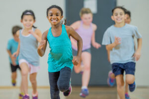 Children in Phys. Ed. class in gym clothes running and smiling