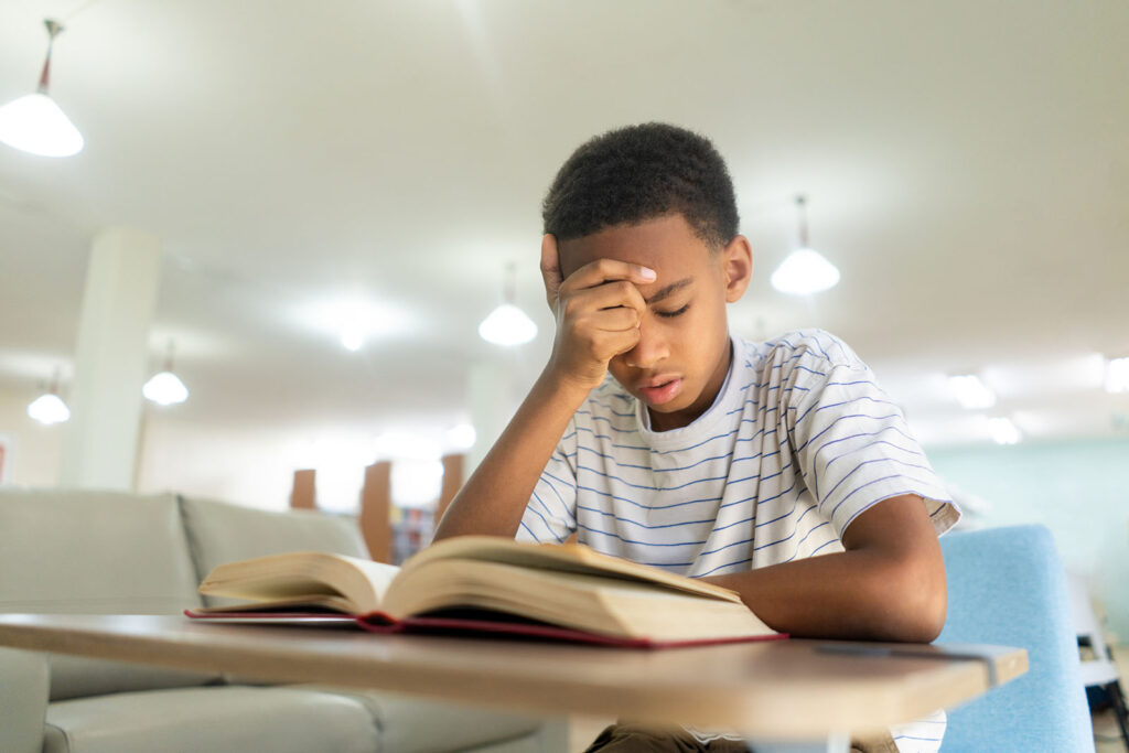 Child with hand on forehead in visible frustration reading a book on a desk